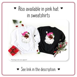 May include: Two sweatshirts with a black Santa Claus with a pink hat and white beard design. One sweatshirt is white and the other is black. The text "Also available in pink hat in sweatshirts" and "See link in the description" is visible in the image.