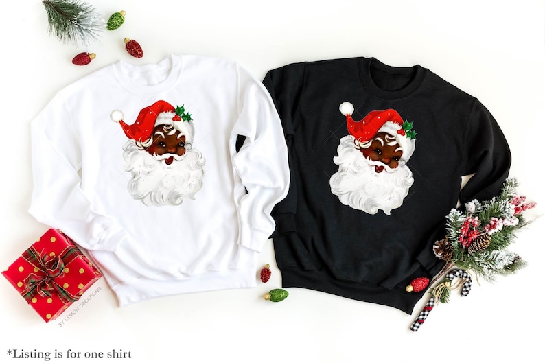 May include: Two Christmas sweatshirts, one white and one black, feature a vintage illustration of a Black Santa Claus with a red hat and white beard.