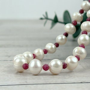May include: A white pearl necklace with small red ruby beads interspersed between the pearls.
