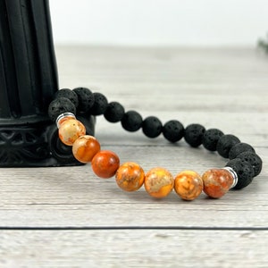 May include: A bracelet made with black lava rock beads and orange and white jasper beads.