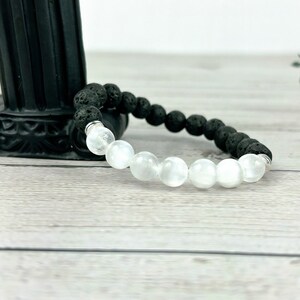 May include: A black lava rock and white moonstone beaded bracelet. The bracelet is made with natural stones and has a silver metal clasp.