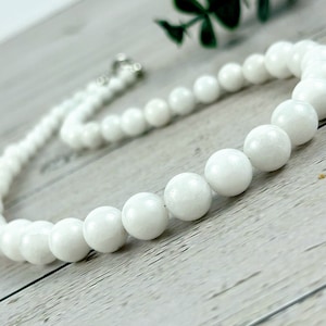 May include: White gemstone bead necklace with a silver clasp. The necklace is made of round, smooth beads.