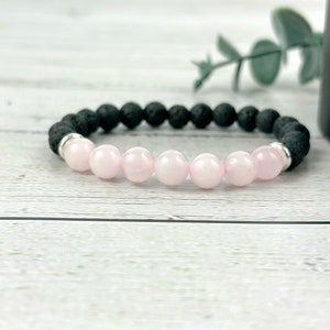 May include: A bracelet made of black lava rock beads and pink rose quartz beads. The bracelet has silver spacers between the beads.
