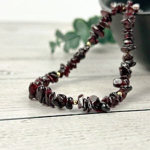 May include: A red gemstone chip bracelet with gold accents. The bracelet is made of small, irregular shaped chips of red gemstone, strung together with gold beads.