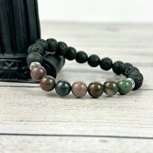 May include: A black lava rock bracelet with a silver spacer and six multi-colored agate beads. The beads are green, brown, and pink.