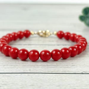 May include: A red coral bead bracelet with a gold clasp. The bracelet is made of round, smooth beads.