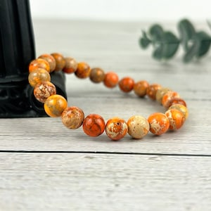May include: A bracelet made of orange and white jasper beads. The beads are round and have a speckled pattern.