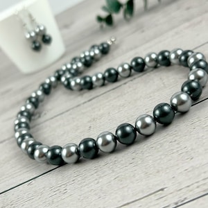 May include: A silver and black pearl necklace and earrings set. The necklace is made of alternating silver and black pearls. The earrings are simple silver posts with a single black pearl.