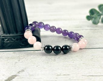 May include: A bracelet made with amethyst, rose quartz, and black onyx beads. The beads are strung on a silver cord.