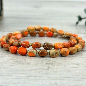 May include: A double-strand necklace made with orange and brown jasper beads. The beads are oval-shaped and have a marbled pattern.