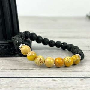 May include: A black lava rock bracelet with yellow and brown jasper beads. The bracelet is made with 8mm beads and has a silver metal clasp.
