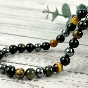 May include: A beaded bracelet with black, gold, and silver beads. The bracelet is made of natural stones and is designed for men or women.