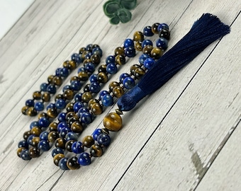 May include: A blue and gold beaded mala necklace with a blue tassel. The necklace is made of tiger's eye and lapis lazuli beads.