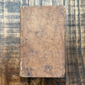 May include: A vintage, brown leather-bound book with a worn and aged appearance. The cover is textured and shows signs of use over time.