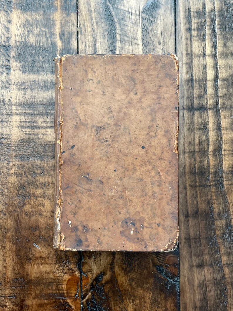 May include: A vintage, brown leather-bound book with a worn and aged appearance. The cover is textured and shows signs of use over time.