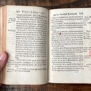 May include: An open book with yellowed pages and a brown leather cover. The book is open to a page with the title "Description" and text in French about the island of Jamaica. The next page is titled "De la Grande Bretagne" and contains text about the island of Cumberland.