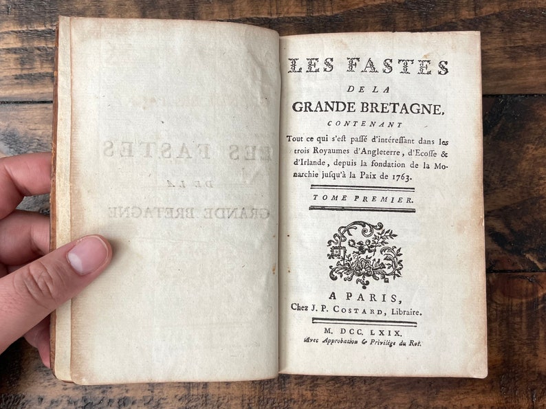 May include: A vintage book titled "Les Fastes de la Grande Bretagne" with the text "Tome Premier" and "A Paris, Chez J.P. Costard, Libraire. M. DCC. LXIX, avec Approbation & Privilige du Rot."