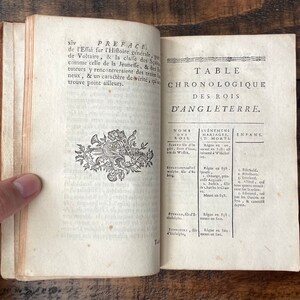 May include: An open book with a decorative design on the left page and a table of contents for the Kings of England on the right page. The title of the table is "Table Chronologique des Rois d'Angleterre".