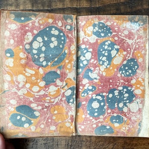May include: The cover of an old book with a marbled paper design in shades of red, blue, and yellow.