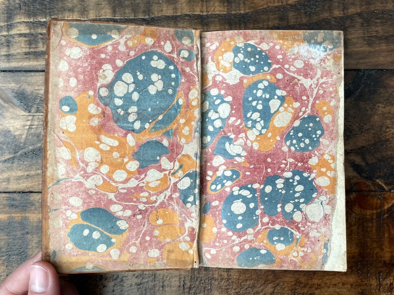 May include: The cover of an old book with a marbled paper design in shades of red, blue, and yellow.