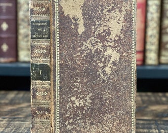 Könnte beinhalten: Ein antikes, braunes, ledergebundenes Buch mit goldenen Verzierungen und dem Titel "HISTORIENS OU VIES DU SECOND AGE" auf dem Rücken. Das Buch liegt auf einer Holzoberfläche.