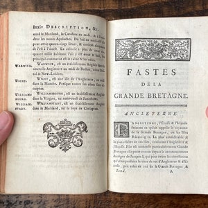 May include: An open book with a title page that reads "Fastes de la Grande Bretagne." The book is open to a page with text in French about the history of England, Scotland, and Ireland. The book is bound in brown leather and has a decorative design on the cover.