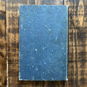 May include: A dark blue hardcover book with a textured cover. The book is slightly worn and has a few white spots on the cover.