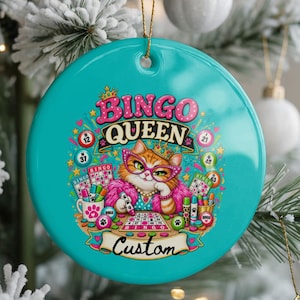May include: A round turquoise ceramic ornament featuring a central illustration of a cat wearing pink glasses and a crown. The text reads BINGO QUEEN and Custom. The cat is surrounded by bingo cards, markers, and paw prints. A gold string is attached.