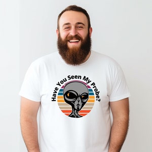 May include: A white t-shirt featuring a retro-style graphic of a grey alien with orange eyes. The graphic reads "Have You Seen My Probe?" in black text.