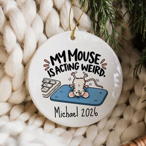 Könnte beinhalten: Ein rundes, weißes Keramikornament mit einer Cartoon-Illustration einer Maus, die kopfüber auf einem blauen Mauspad neben einer Computertastatur liegt. Der Text lautet "MY MOUSE IS ACTING WEIRD." und "Michael 2026" in schwarzer Schrift mit goldener Schnur.