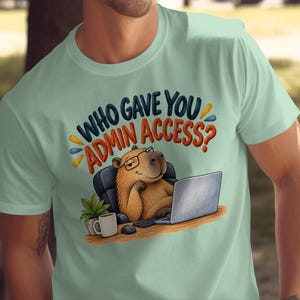 May include: A light green t-shirt featuring a graphic of a capybara wearing glasses, sitting at a desk with a laptop, a coffee mug, and a small plant. The text above the capybara reads, "WHO GAVE YOU ADMIN ACCESS?" in bold, colorful lettering.