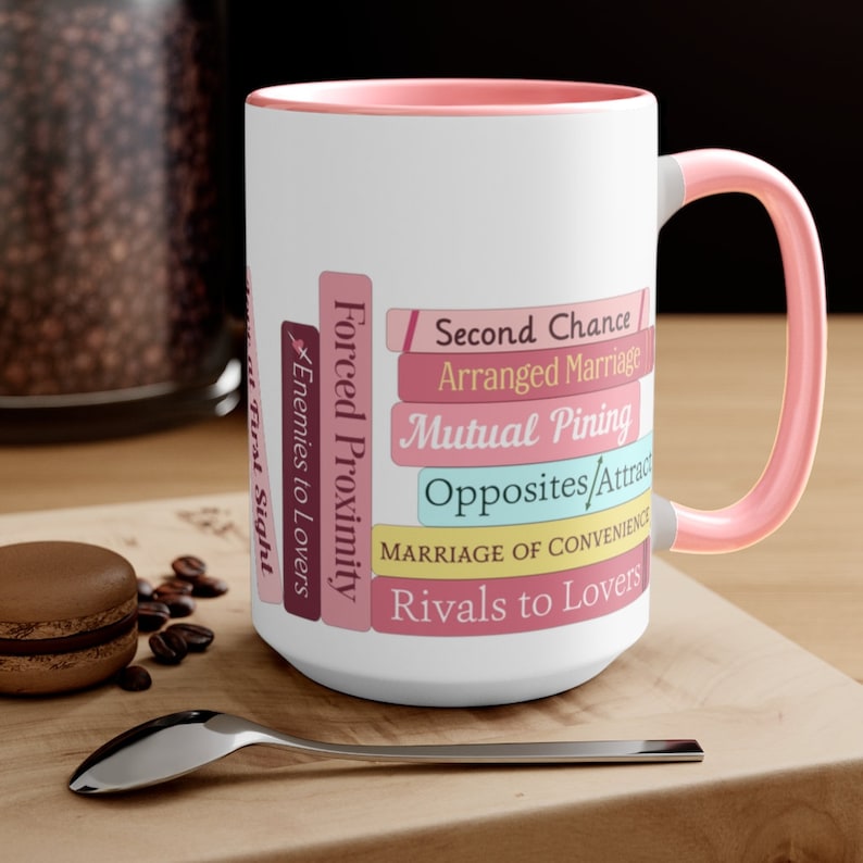 A pink mug on a coffee table with a stack of books on the mug