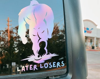 May include: An opal holographic vinyl decal applied to a vehicle window, featuring a silhouette of a large, hairy creature walking away. The design includes the text "LATER LOSERS" in a bold, sans-serif font positioned below the figure.