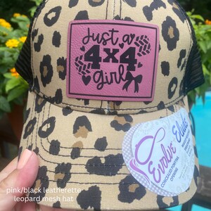 May include: A tan and black leopard print baseball cap with a black mesh back. A square pink patch on the front features the black text Just a 4x4 girl with heart and bow accents. A white sticker on the brim reads Evolve Elude with product details.