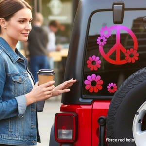 May include: A red Jeep with a black top and a spare tire. The rear window features a peace sign and flower decals in shades of pink and red. The text "fierce red holo" is visible.