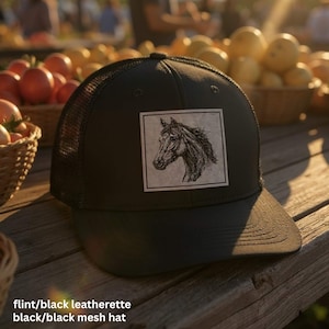 May include: Black trucker hat with a horse head sketch on a square patch. The hat features a black mesh back and a curved brim. The hat is made of flint/black leatherette and black/black mesh.