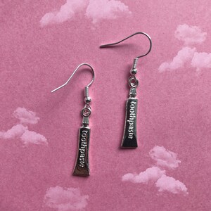 May include: A pair of silver earrings shaped like tubes of toothpaste, each with the word "toothpaste" engraved on the front.