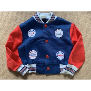 May include: A vintage baseball-themed jacket in navy blue with red sleeves. The jacket features patches for the Sox, Yankees, Athletics, and Rangers teams. It has a white collar and cuffs with red and blue stripes, and red button closures.