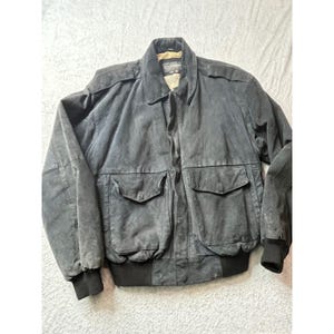 May include: A dark gray suede jacket with a collared neckline, two front pockets, and black ribbed cuffs and hem. The jacket has a classic bomber style and a soft, worn appearance. The brand name is visible on the collar.