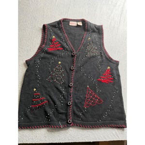May include: A black button-up vest with red trim and Christmas tree designs. The trees are embroidered in red and embellished with beads and sequins. The vest has a V-neck and is sleeveless.