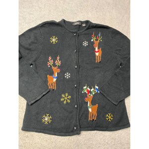 Könnte beinhalten: Dunkelgraue Cardigan-Strickjacke mit Knöpfen und gestickten Rentier- und Schneeflocken-Designs. Die Rentiere haben bunte Geweihe und Schals. Der Pullover ist ein festliches Kleidungsstück.