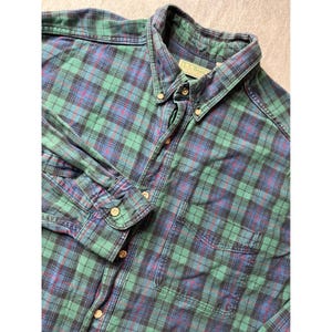 May include: Green, blue, and red plaid button-down shirt. The long-sleeved shirt has a button-down collar, a chest pocket, and buttoned cuffs. The shirt is from the brand L.L. Bean.