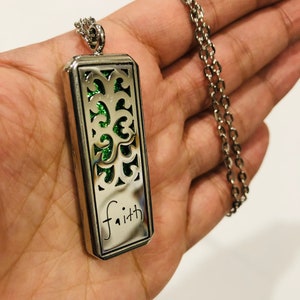 May include: Silver necklace with a rectangular pendant featuring a green glitter design and the word "faith" inscribed on the bottom.