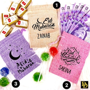 May include: Three burlap gift bags with different designs. The bags are decorated with a crescent moon and the words "Eid Mubarak". The bags are personalized with the names "Zainab", "Sakina", and a third name that is not visible in the image. The bags are surrounded by colorful lollipops.