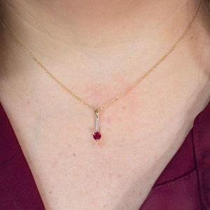 Puede incluir: Un collar de cadena de oro con un colgante que presenta una piedra roja y peque&ntilde;as piedras transparentes.