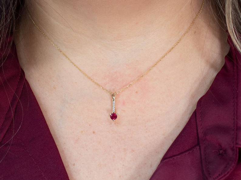 Puede incluir: Un collar de cadena de oro con un colgante que presenta una piedra roja y peque&ntilde;as piedras transparentes.