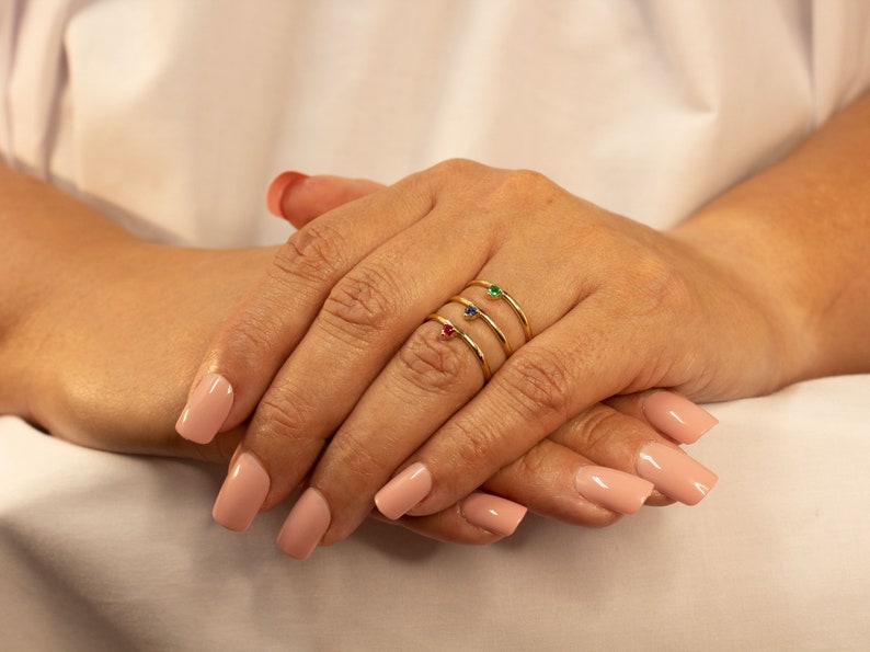 Peut inclure: Trois bagues en or avec de petites pierres pr&eacute;cieuses. Les bagues sont empil&eacute;es sur un doigt. Les pierres pr&eacute;cieuses sont rouge, bleu et vert.