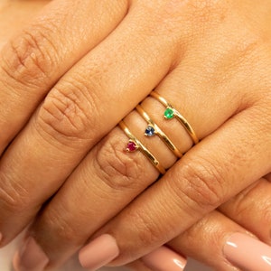 Peut inclure: Trois bagues en or avec de petites pierres pr&eacute;cieuses. La bague du haut a une pierre pr&eacute;cieuse verte, la bague du milieu a une pierre pr&eacute;cieuse bleue et la bague du bas a une pierre pr&eacute;cieuse rouge.