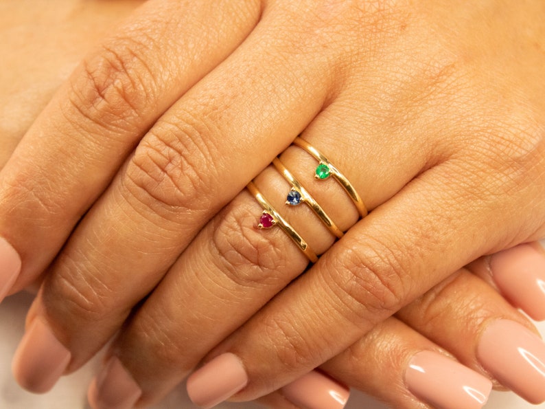 Peut inclure: Trois bagues en or avec de petites pierres pr&eacute;cieuses. La bague du haut a une pierre pr&eacute;cieuse verte, la bague du milieu a une pierre pr&eacute;cieuse bleue et la bague du bas a une pierre pr&eacute;cieuse rouge.