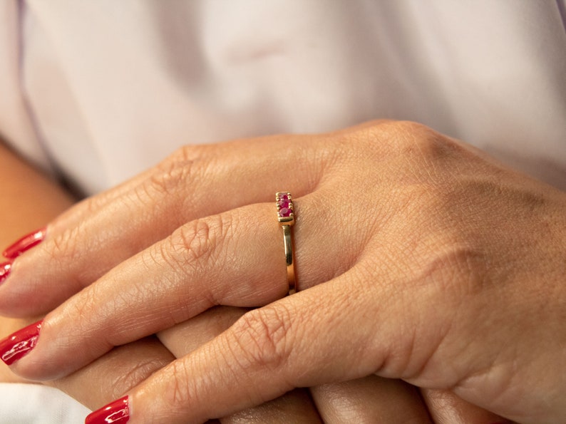 Pu&ograve; includere: Un anello d'oro con una fila di piccole pietre preziose rosse.